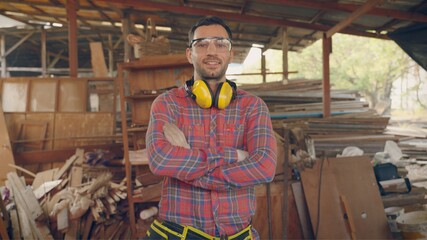 Caucasian portrait of worker craftsman or carpenter man standing with confidence and awesome smart face with background of wood wall factory with white smoke and daylight.