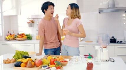 Asian couple feed each other while cooking together in modern kitchen enjoy conversation and healthy vegetarian salad food preparation. Lifestyle, happy homeowners, romantic date, hobby, love concept.