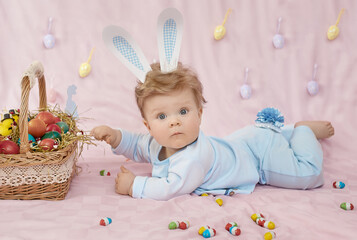 Cute baby wearing a blue bunny rabbit costume lying on his stomach near the basket of Easter eggs. Happy Easter time