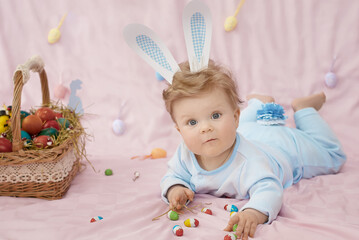 Cute little baby in bunny costume looking on us, he is wearing a blue bunny rabbit costume lying on his stomach. Happy Easter time