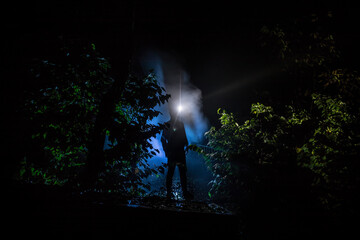 strange light in a dark forest at night. Silhouette of person standing in the dark forest with light. Horror halloween concept. strange silhouette in a dark spooky forest at night