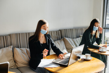 A group of masked girls keep a social distance in a cafe when working on laptops.