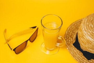 concept of relaxation and thirst on the beach. a glass of lemonade on a yellow background with sunglasses and a straw hat. top view