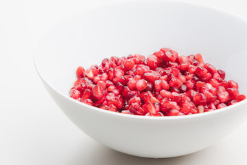 Close up detail of superfood pomegranate seeds in a white bowl on a plain white surface and background.