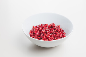 Superfood pomegranate seeds in a white bowl on a plain white surface and background.