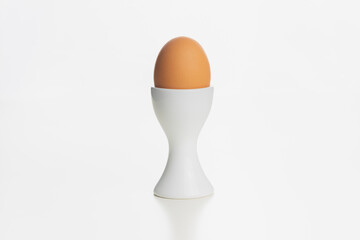 A brown farm egg in a white egg cup isolated on a plain white surface and background.