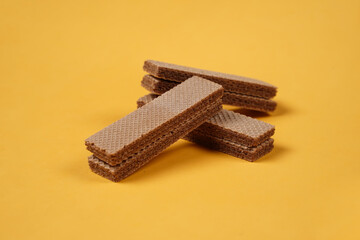 Random pile of wafers isolated on a yellow background. Chocolate biscuit wafers filled with delicious creamy chocolate. Dry and crispy wafers ready to eat. Ready to start the day with a wafer.
