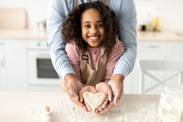 Happy black man and girl holding dough in heart shape