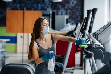 Fototapeta premium The girl in the mask disinfecting the gym equipment during a pandemic.