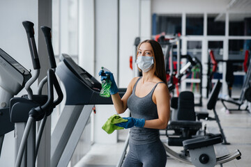 Fototapeta premium The girl in the mask disinfecting the gym equipment during a pandemic.