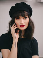 Indoor close up portrait of young beautiful fashionable woman red lips wearing black beret and t-shirt french inspired fashion concept