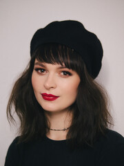 Indoor close up portrait of young beautiful fashionable woman red lips wearing black beret and t-shirt french inspired fashion concept