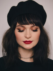 Indoor close up portrait of young beautiful fashionable woman red lips wearing black beret and t-shirt french inspired fashion concept
