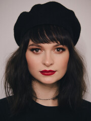 Indoor close up portrait of young beautiful fashionable woman red lips wearing black beret and t-shirt french inspired fashion concept