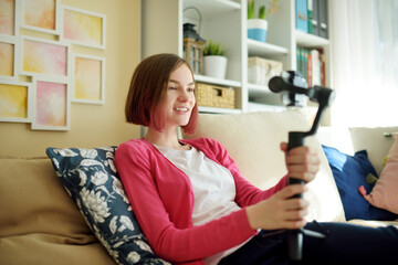Fototapeta na wymiar Beautiful teenage girl recording video blog with her smartphone. Young vlogger shooting vlog at home. Teen influencer creating content for her social media account.