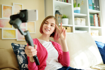 Beautiful teenage girl recording video blog with her smartphone. Young vlogger shooting vlog at home. Teen influencer creating content for her social media account.