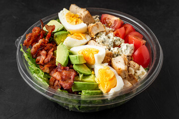 Healthy cobb salad in plastic package for take away or food delivery on black background. close up. low carb