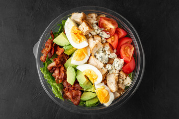 Plastic package with healthy cobb salad with chicken, avocado, bacon, blue cheese, tomatoes and eggs to take away