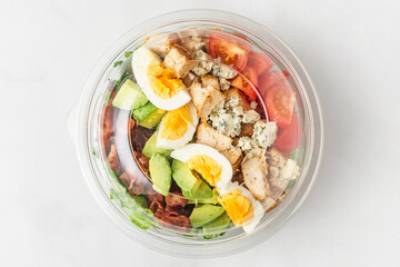 Plastic package with healthy cobb salad with chicken, avocado, bacon, blue cheese, tomatoes and eggs to take away