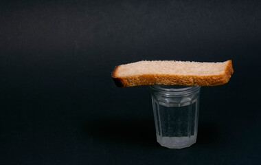 Glass of vodka and a piece of bread on a black background