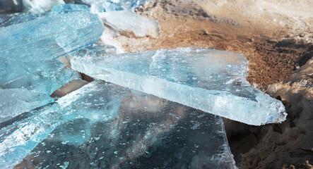chunks of crystal clear ice on the frozen sandy shore contrast of blue ice and yellow sand