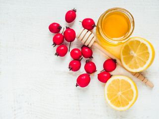 Fresh yellow lemon, jug of honey and red berries on a white wooden table. Top view, close-up, isolated. Concept of preventing colds