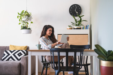 Beautiful business woman working from home. Smiling businesswoman having online meeting, she is using video call on digital tablet while sitting in living room