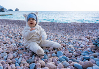 10-month-old baby plays with pebbles sitting on the beach in winter and listens carefully to mom