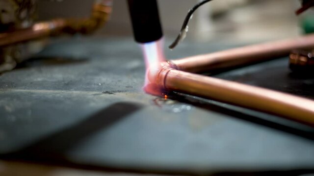 Flame from a gas blowtorch being applied to a copper pipe fitting, to melt solder and seal the joint.