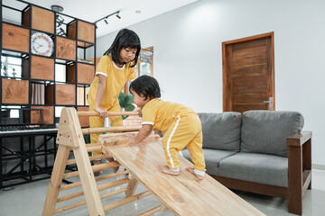 The baby climbs a pikler triangle toy accompanied by a sister in the living room