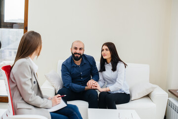 Naklejka na ściany i meble A young happy married couple of men and women talk to a psychologist at a therapy session. Psychology.