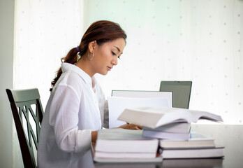 Beautiful Asian student women reading book and using notebook working from home for social distance and self responsibility concept