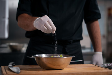 Fototapeta na wymiar chef cook hands in gloves adding salt in greek salad at restaurant kitchen