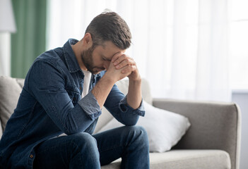 Depressed man sitting on couch in living room