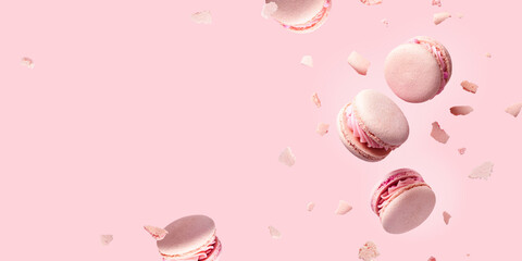 French macarons flying in the air among the crumbs on pink background. Levitation concept. food background with copyspace.wide banner