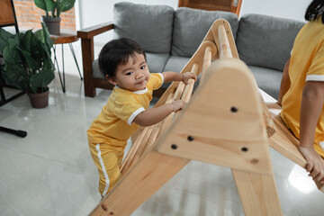 little kids climb on the pikler triangle toy while playing together in the living room
