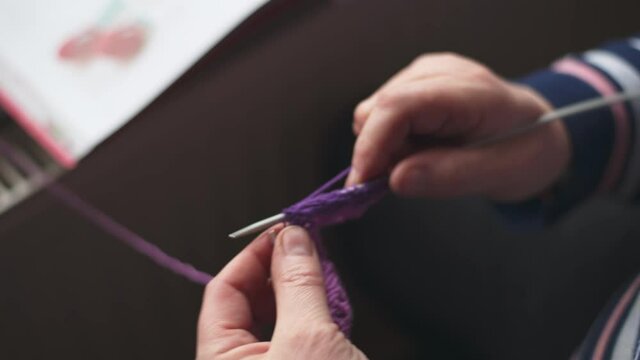 close up of woman knitting with purple whool at home to create a doll. focus on knitting needle