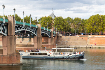 Un bateau sous le pont Saint-Pierre de Toulouse qui enjambe la Garonne et relie la place Saint-Pierre à l'hospice de la Grave - obrazy, fototapety, plakaty