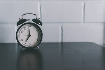 Black vintage alarm clock on brown wooden table and white cement wall background, Time concept.