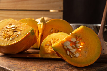 Pumpkin, rustic arrangement with pumpkin cut into pieces, knife, board, wooden spoon, iron pot on a table, with rustic fabric and wood, black background, selective focus.