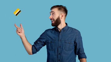 Millennial hipster guy catching credit card on blue studio background, panorama. Contactless...