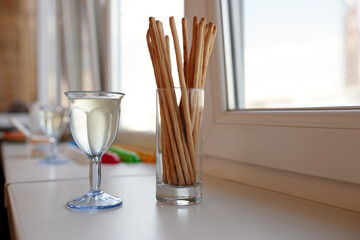 blue glass of white wine and bread sticks grissini on a table next to the windows with day light. Lunch time appetizer. Copy space