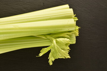 One light green, natural, juicy celery stalk on a slate board, close-up, top view.