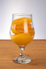 Peaches in syrup placed in bowl on wooden mat, gray gradient background, selective focus.