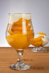 Peaches in syrup placed in two bowls covered with sour cream on wooden mat, gray gradient background, selective focus.