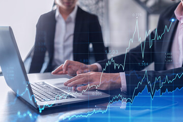 Two traders man and woman researching historic data to predict stock market behavior using laptop. Internet trading concept. Forex and financial hologram chart. Forecasting and planning.