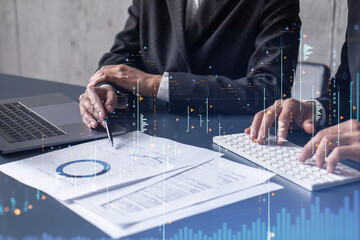 Two traders man and woman researching historic data to predict stock market behavior. Internet trading concept. Forex and financial hologram chart over the table with the documents