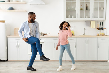 Black dad and daughter singing and dancing while cooking together