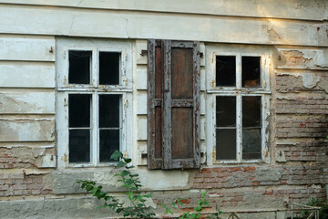 Close-up of two weathering windows of a decaying white house facade

