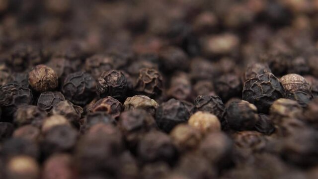 Grains of black pepper fall into a heap in slow motion. Peppercorn close-up. Macro shot